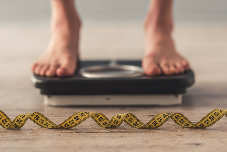 person standing on a scale with a tape measure laying in front